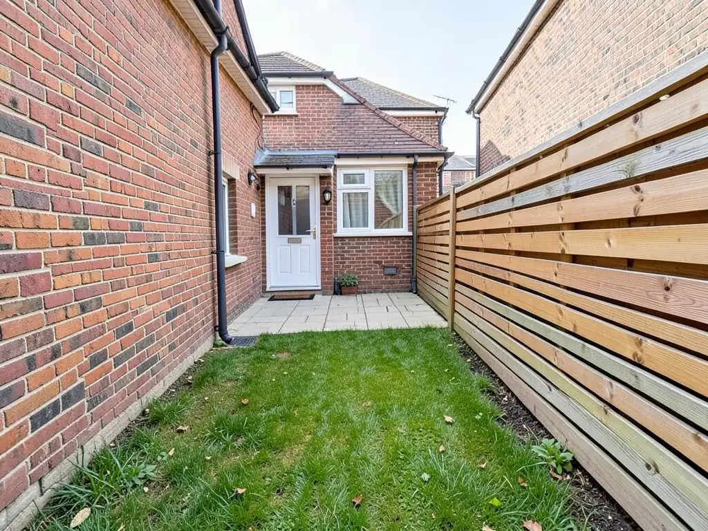 AI-generated example: a small narrow lawn between a red brick house wall and a horizontal slat wooden fence, with a small area of light pavers by a white back door, a door mat and a small potted plant