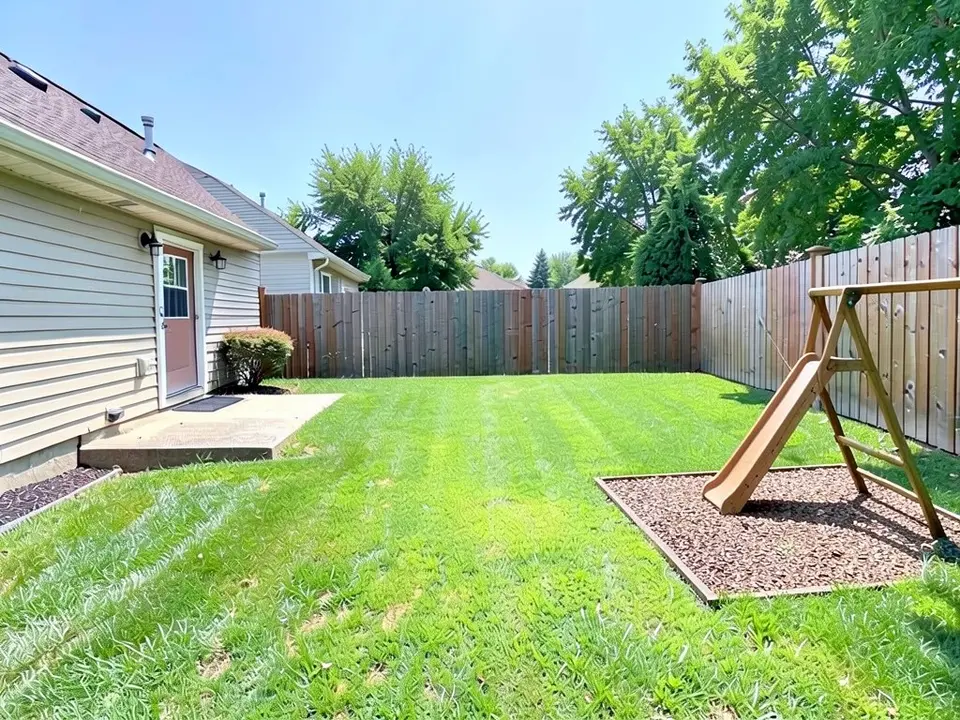 AI-edited version of the same image: at the far right of the lawn a wooden swing-set frame with a slide stands on a square of dark wood chips with a timber border, cut off by the right edge of the picture