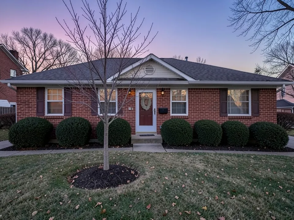 AI-generated example: a one-story red brick ranch house at dusk with dark shutters, a red front door with a wreath, a row of round boxwood shrubs, a small bare tree in a mulch ring and a lawn with fallen leaves