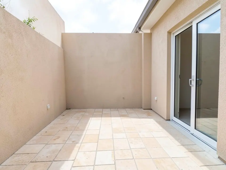 AI-generated example: an empty courtyard with light beige stone paving, a beige stucco wall at the back and on the left, a large sliding glass door on the right with a white frame, a small socket on each side wall and a plant showing over the top of the left wall, in daylight