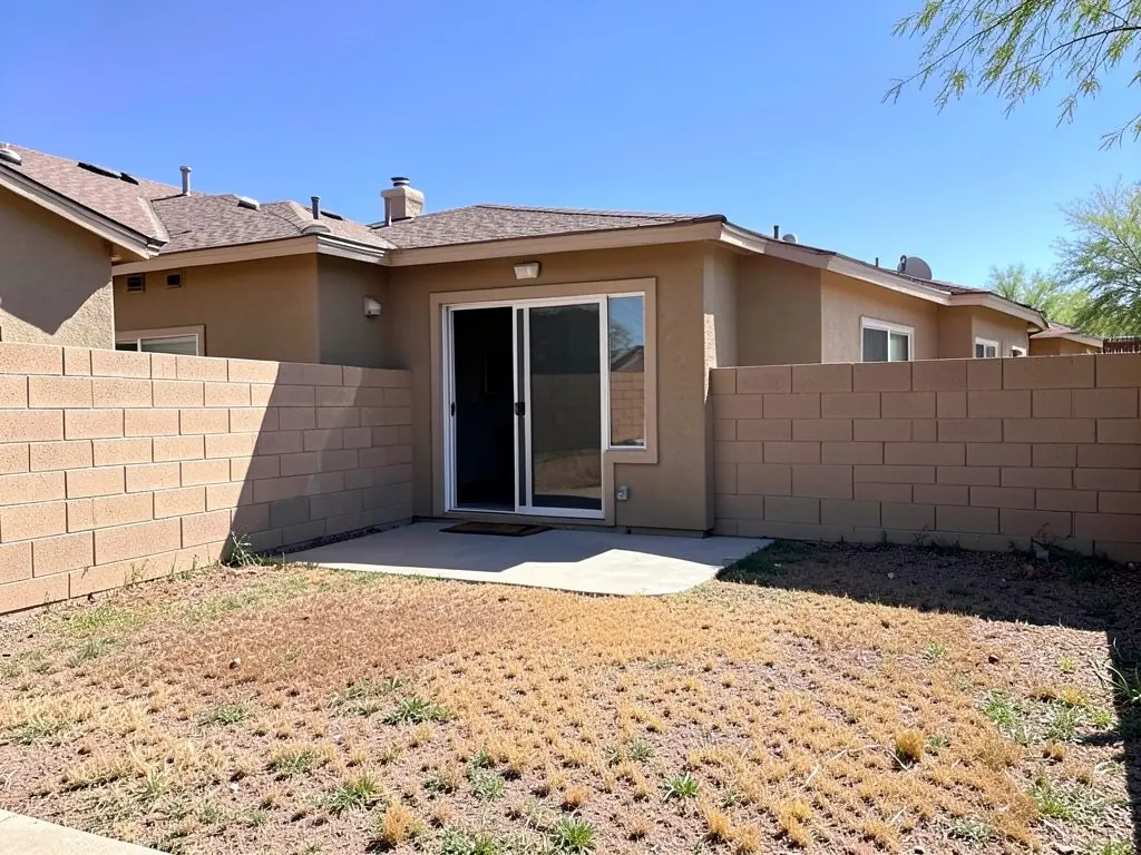 AI-generated example: the back of a one-story tan stucco house with a sliding glass door and a small concrete slab, a brown dead lawn and a tan concrete block wall around the yard