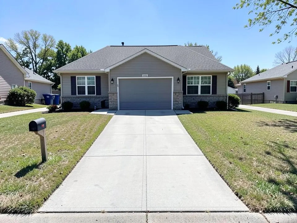 AI-generated example: a house with a stone base and a one-car garage with a grey door, a straight grey concrete driveway running toward the street, a mailbox on the left and mown dry-looking lawn on both sides of the drive, under a blue sky