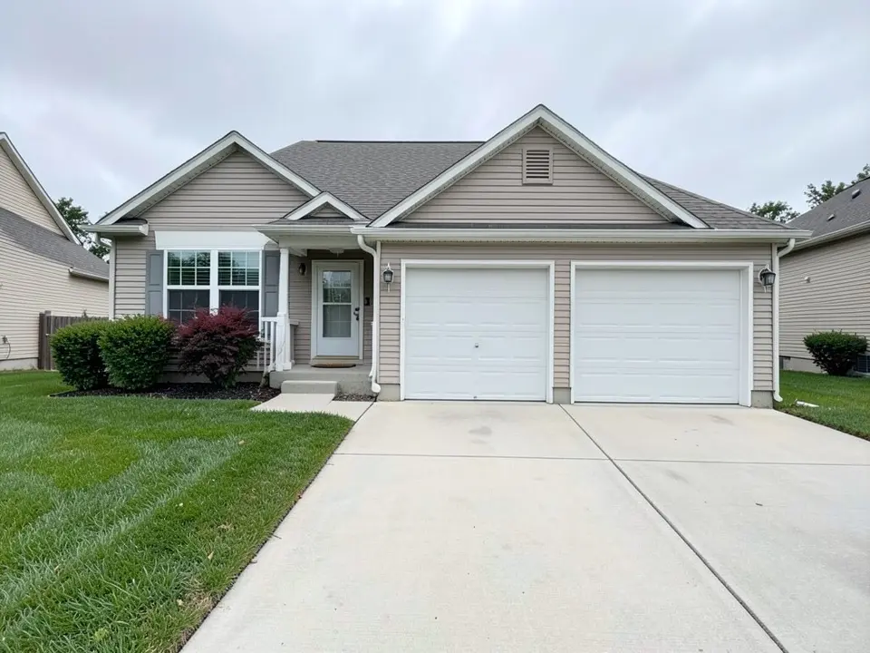 AI-generated example: a beige house with a two-car garage with white doors, a front door and porch with shrubs including one with red leaves, a wide concrete driveway and a plain mown lawn along its left side under an overcast sky