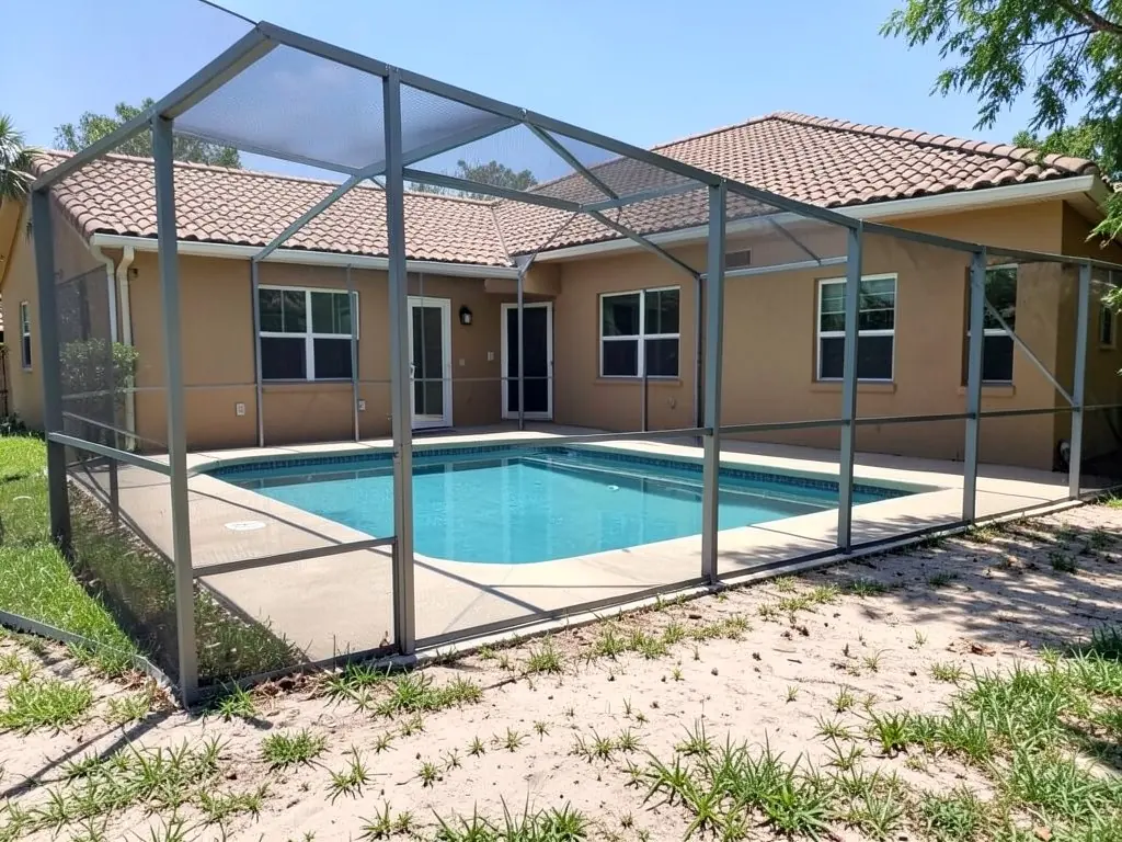 AI-generated example: a screened pool enclosure with a grey aluminum frame around a rectangular pool and concrete deck, behind a one-story tan stucco house with a terracotta tile roof, with a strip of sandy soil and grass tufts in the foreground