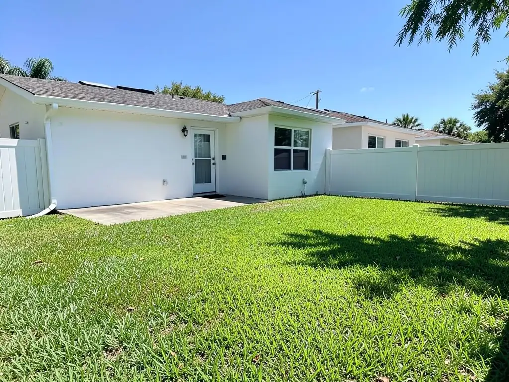 AI-generated example: a one-story white stucco house with a back door and a small concrete patio, a large green St. Augustine lawn and a white vinyl privacy fence