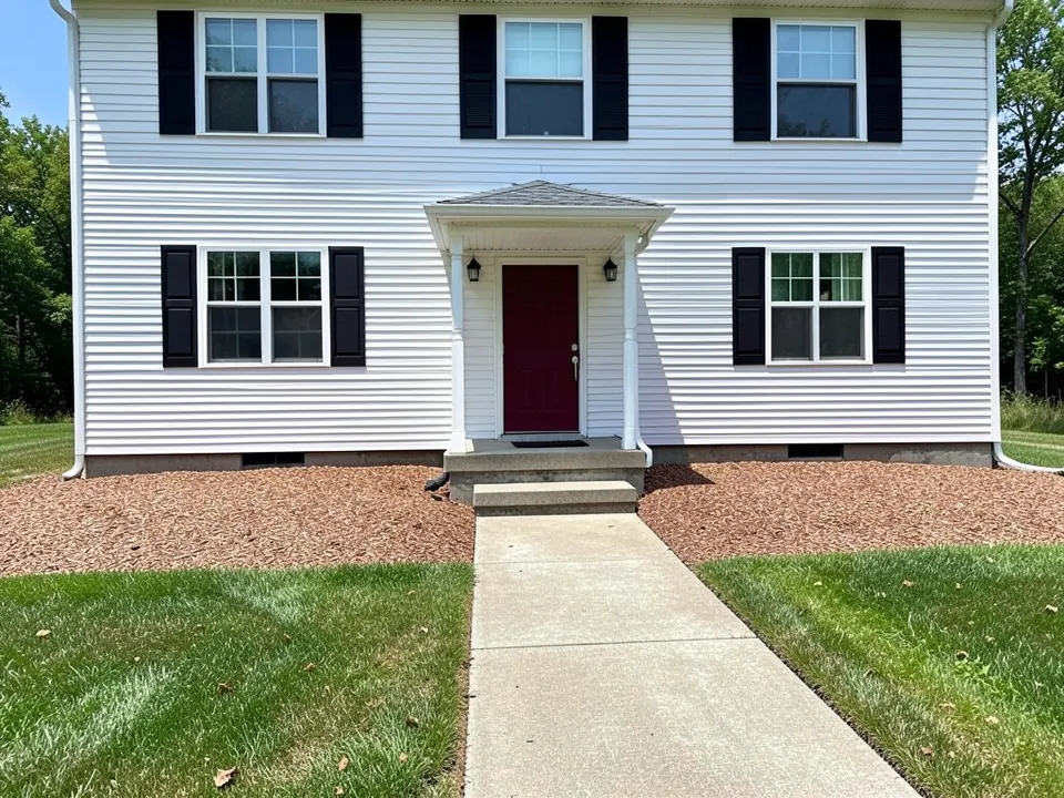 AI-generated example: front of a two-story white house with black shutters and a dark red door, with an empty strip of brown bark mulch along the foundation on both sides of the walkway