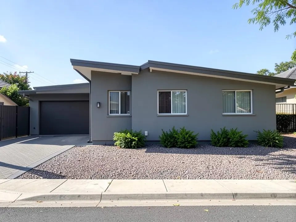 AI-generated example: a modern grey single-storey house with a flat roof and a dark garage door, a front yard of gravel with a few low shrubs, a sidewalk and a driveway on the left, and no fence