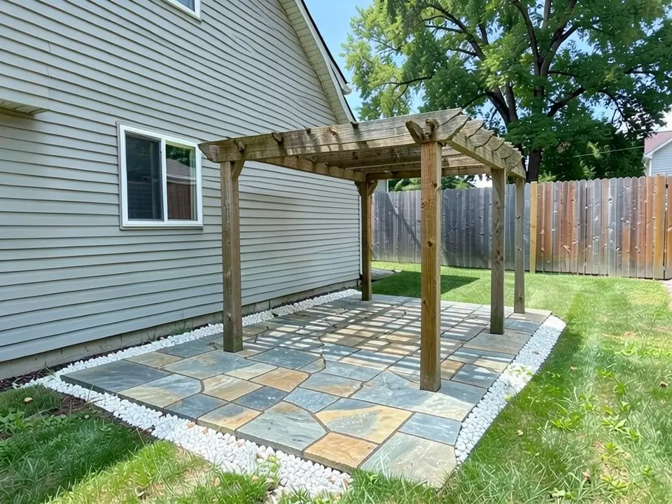AI-edited version of the same image: a flagstone patio of irregular grey, blue-grey and tan stones beside the house wall, under a natural wood pergola, edged with white gravel on three sides, with lawn left around it