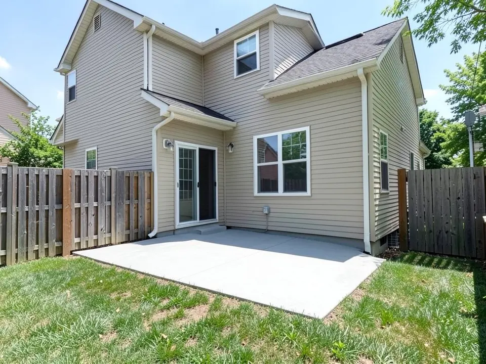 AI-generated example: the back of a beige two-story house with a plain grey concrete patio slab along the wall, a sliding glass door and a large window, weathered wooden fences on both sides and a patchy lawn in front