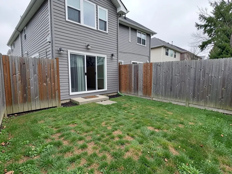 Small fenced backyard behind a gray two-story townhouse with a sliding glass door and a patchy, thin lawn