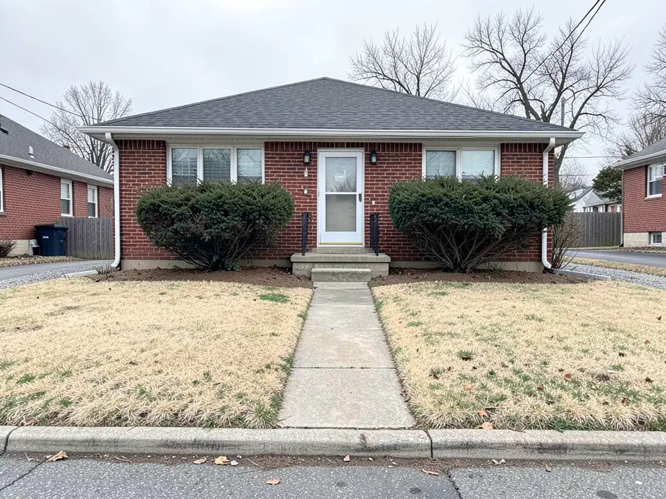 Small red brick bungalow with a patchy yellow lawn, a straight concrete walkway and two overgrown shrubs against the front wall