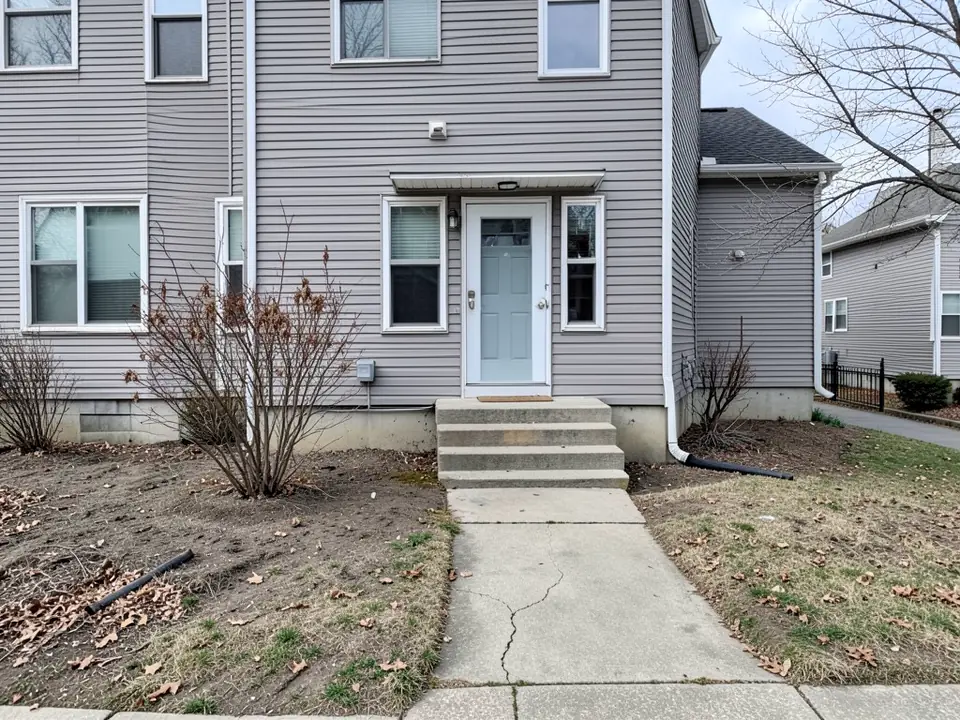 Narrow gray townhouse with concrete steps, a tiny front yard of bare dirt and dead grass and a cracked concrete path