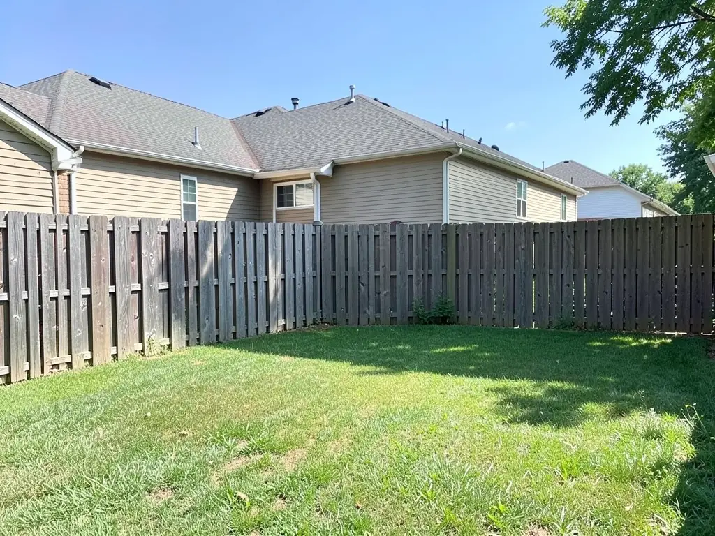 AI-generated example: a plain mown lawn in front of a weathered wooden privacy fence, behind a beige single-story house with a grey roof, with a tree at the top right