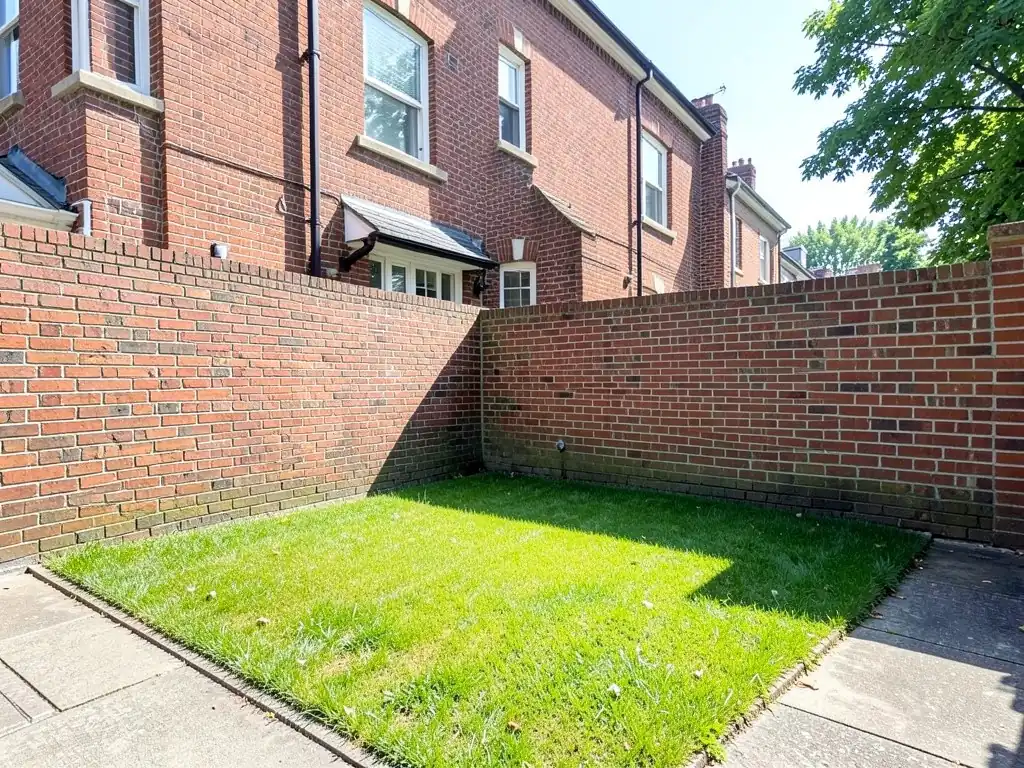AI-generated example: a small square lawn behind a red brick townhouse, enclosed by a tall red brick wall, with stone paving along two sides of the lawn