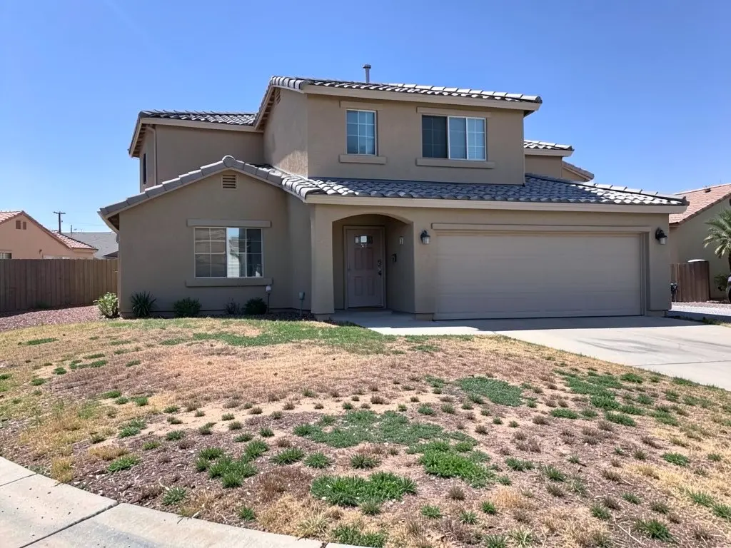 Two-story beige stucco house with a patchy, half-dead grass lawn in a dry suburb